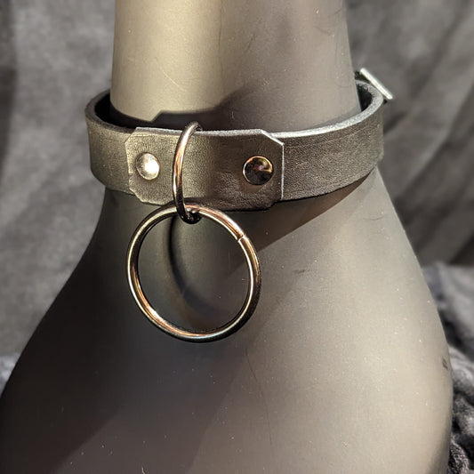 Black leather collar by Smell My Leather. Simple single layer of leather with a 1.5" dangling O-Ring. This collar has gunmetal color hardware.