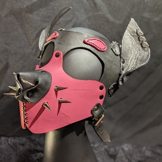 Handmade puphood with a black base color and bright bubblegum pink muzzle and eyebrow and 1 inch silver treecone spike whiskers.. You can see the front left side of the hood, including the septum and ear piercings,  in this image.